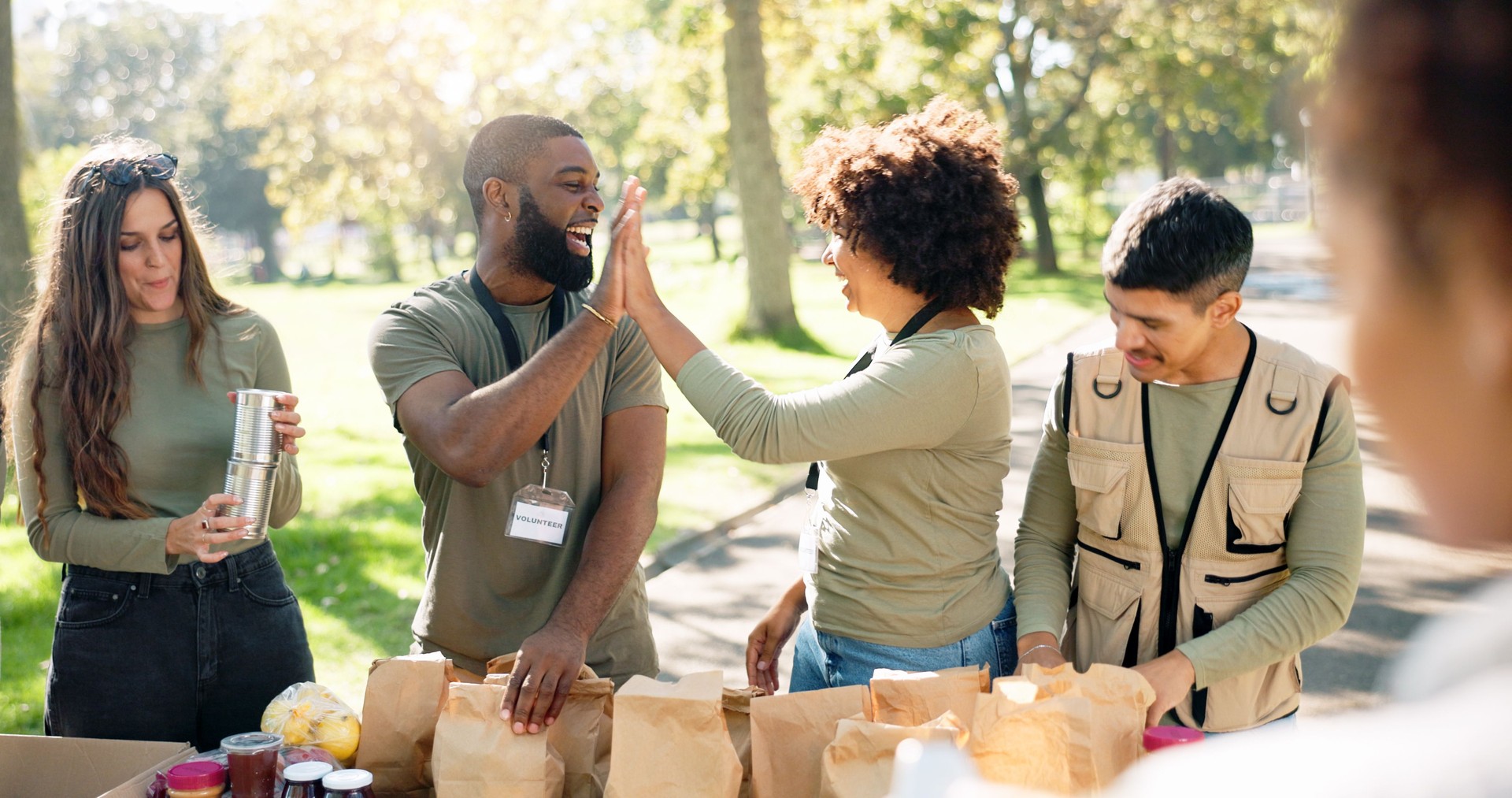 Œuvre de charité, high five et équipe de bénévoles dans le parc avec un colis pour le don, la distribution ou le service communautaire. ONG, diversité et personnes heureuses avec un lot pour le travail d’équipe, la gentillesse ou la responsabilit�