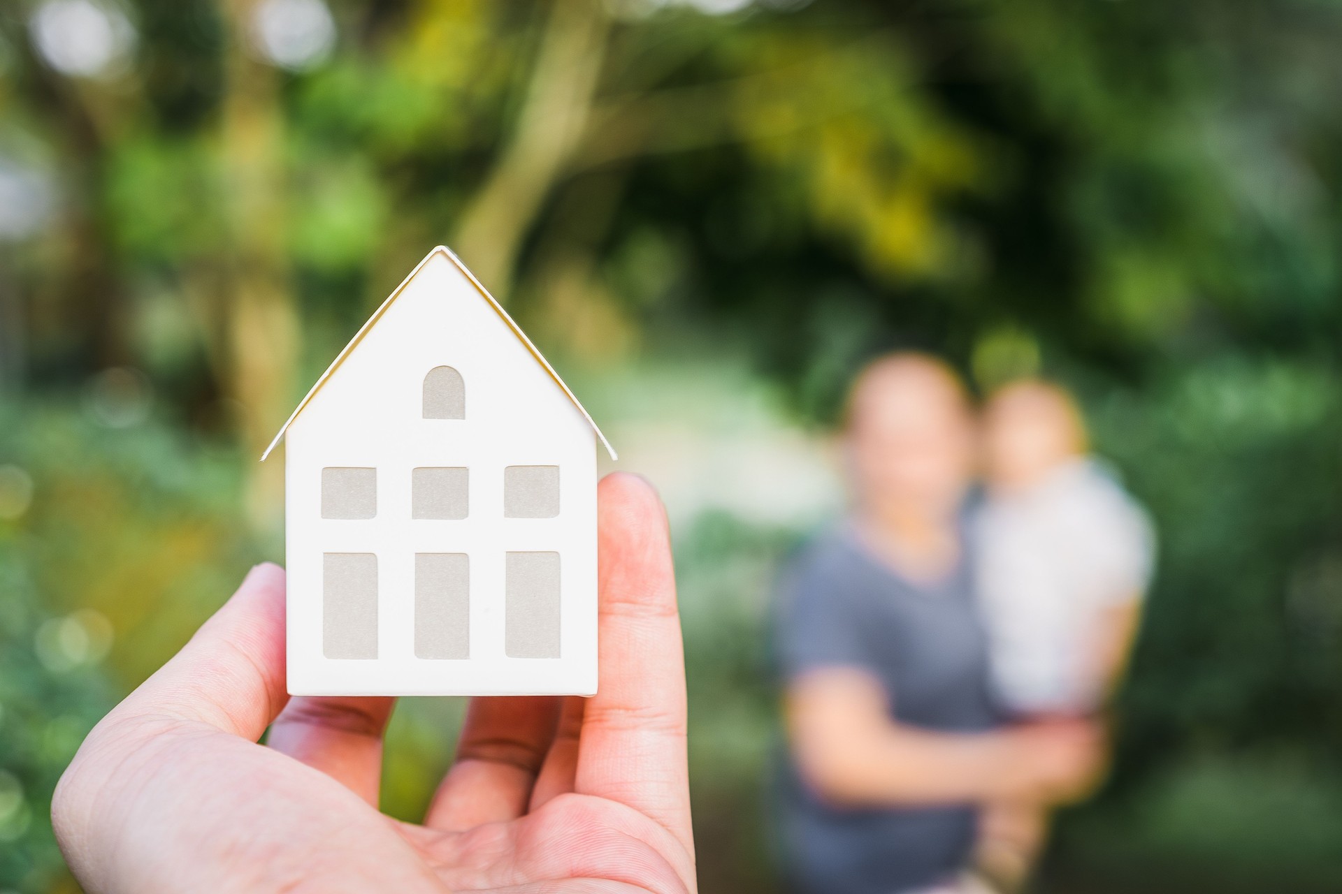 Modèle de maison dans la main d’un agent de courtier d’assurance habitation avec des antécédents familiaux flous. Agent immobilier offre des concepts d’assurance maison, propriété.